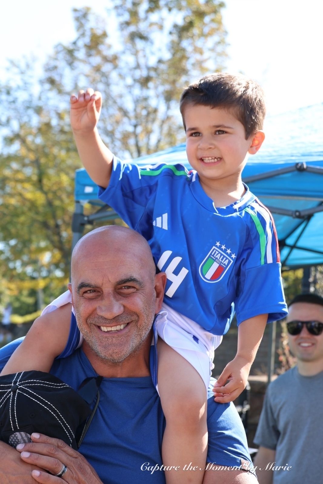 A young supporter in an Italia jersey rides on his grandfather's shoulders at the 2025 Finals Celebration.